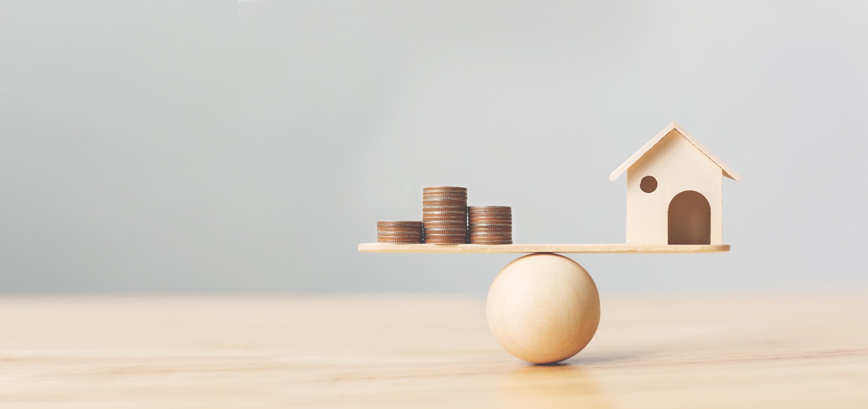 Miniature house and coins balancing on top of a wooden ball